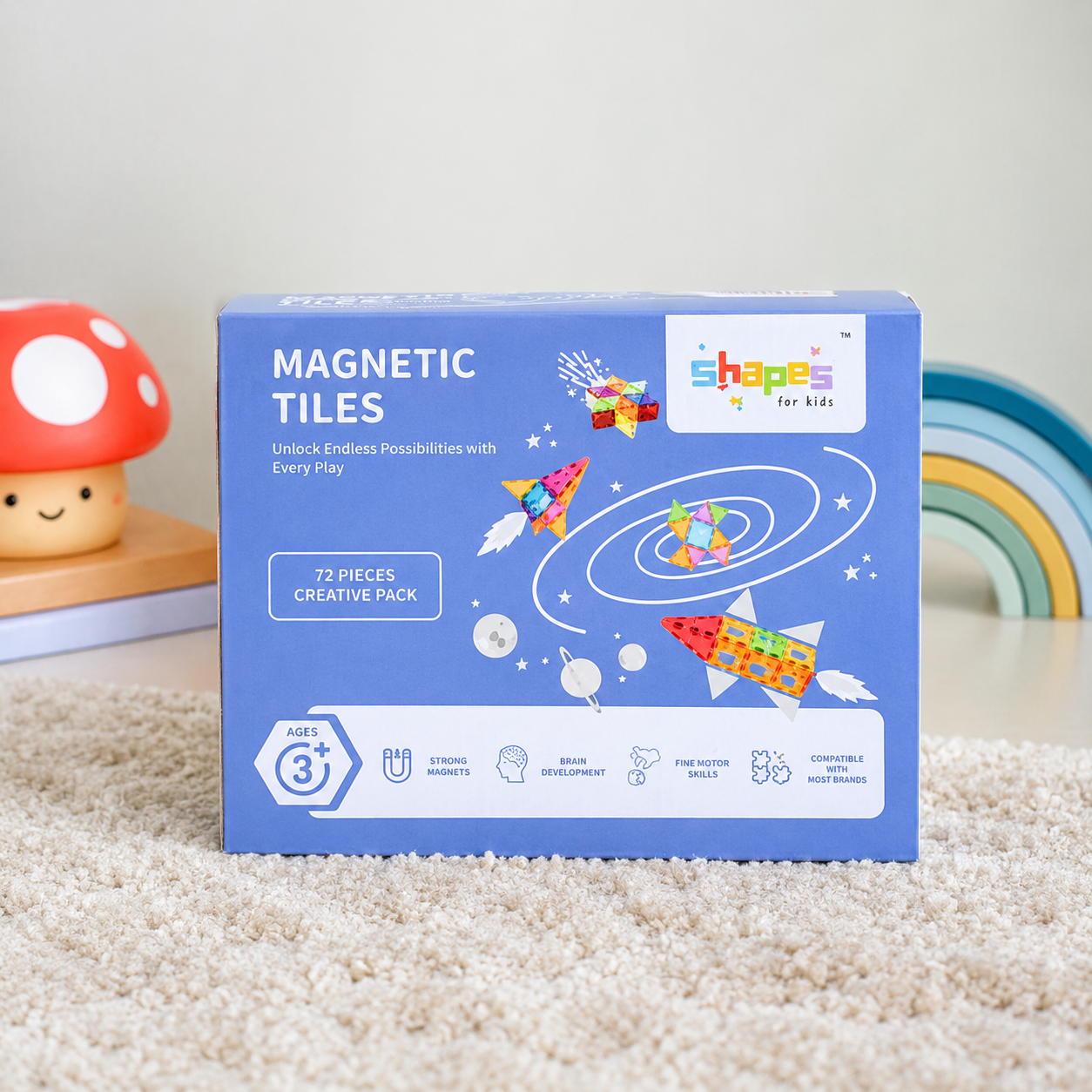 A blue box of Shapes for Kids Magnetic Tiles, 72-piece creative pack, displayed on a beige carpet with a mushroom toy and rainbow in the background.