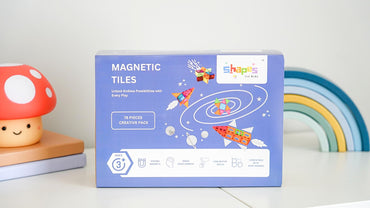 Packaging box of Shapes for Kids magnetic tiles featuring various shapes and colors with a strong magnet label, placed on a wooden surface.