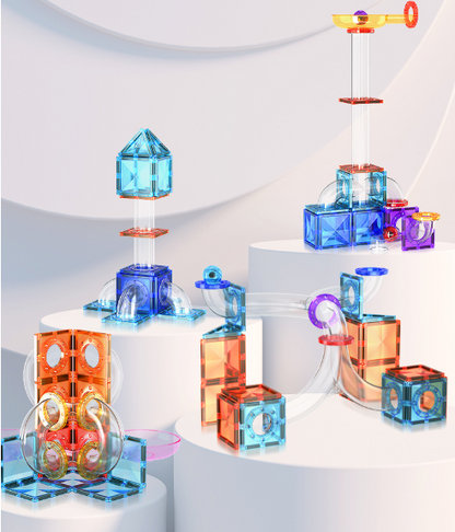 A set of colorful transparent magnetic building blocks arranged in various structures on white display pedestals against a soft light gray studio background.