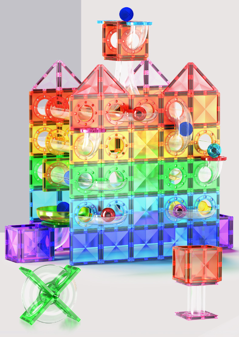 A colorful magnetic building toy set arranged in a castle-like structure, with translucent rainbow tiles, small balls, and accessories on a light gray studio background.