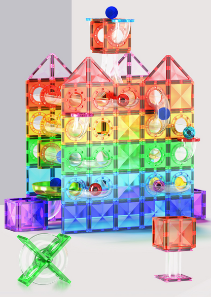 A colorful magnetic building toy set arranged in a castle-like structure, with translucent rainbow tiles, small balls, and accessories on a light gray studio background.